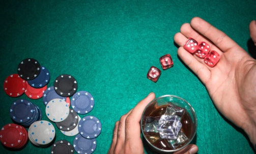 poker-player-showing-red-dices-with-glass-whiskey-poker-table_23-2147881222